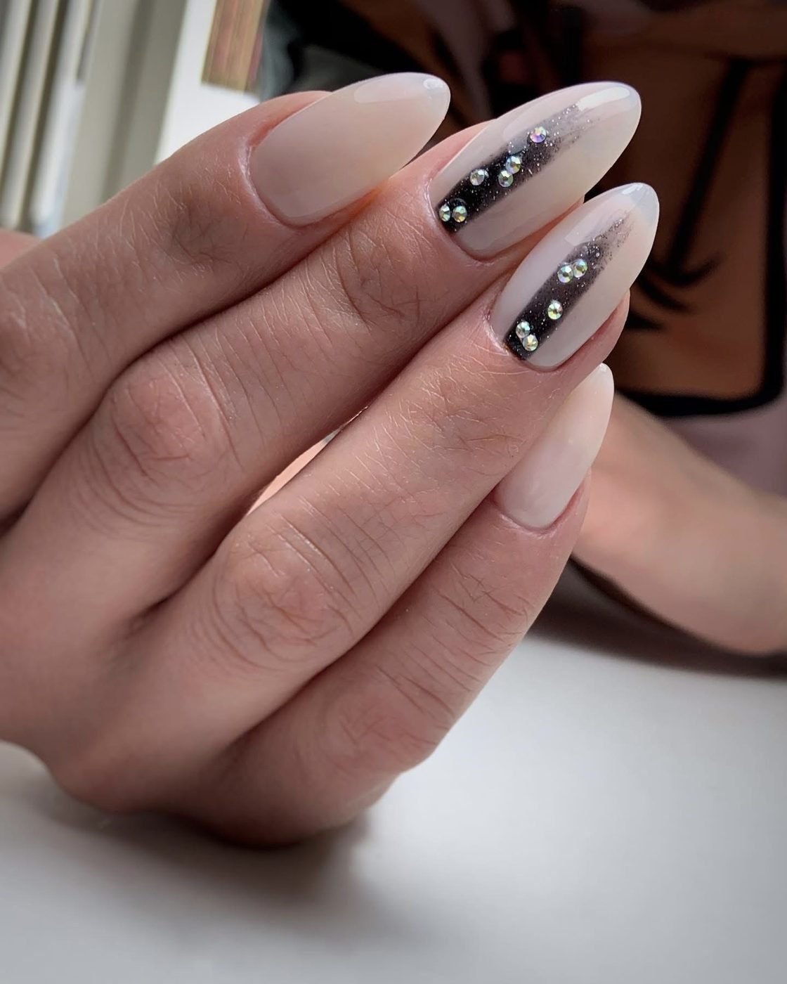 Sheer almond nails with a dark accent nail and small pearls